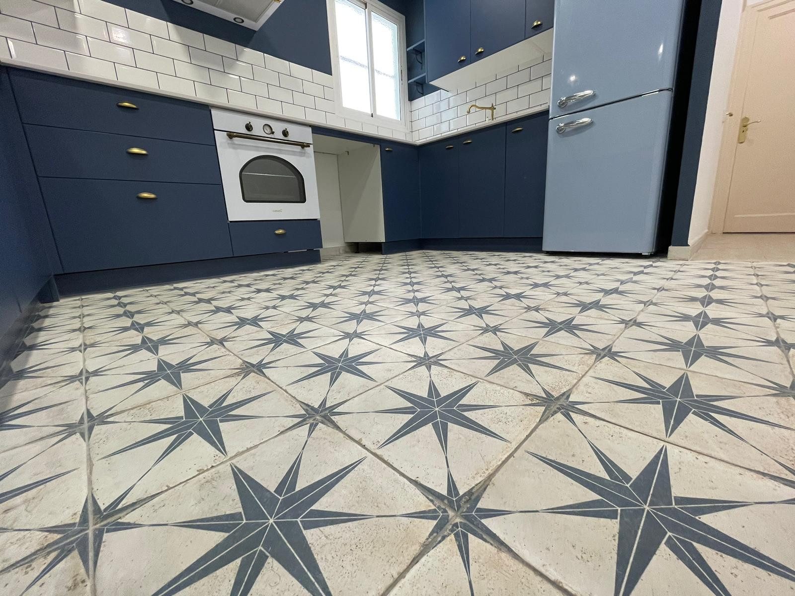 Cocina con muebles azul marino, grifería de latón y suelo hidráulico de estrellas en el Raval, Barcelona
