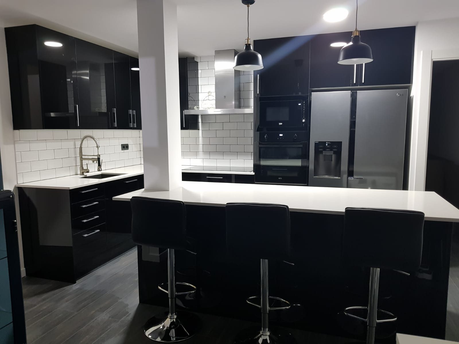 Cocina con acabados en negro brillante, azulejo metro blanco y barra con taburetes en Barcelona