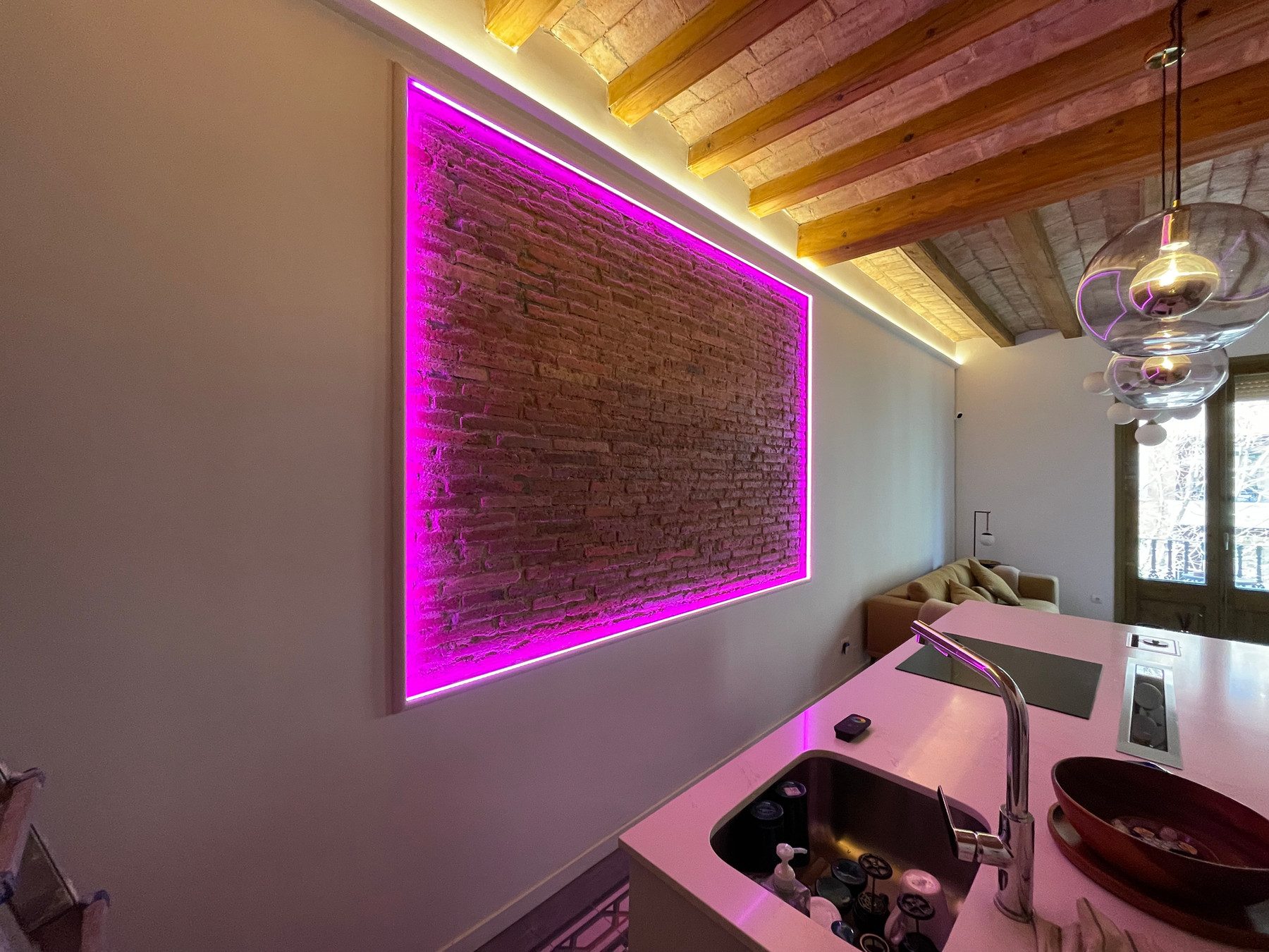 Pared de obra vista con marco de luz LED bajo el techo de vigas de madera de una reforma integral en Carrer Viladomat, Barcelona