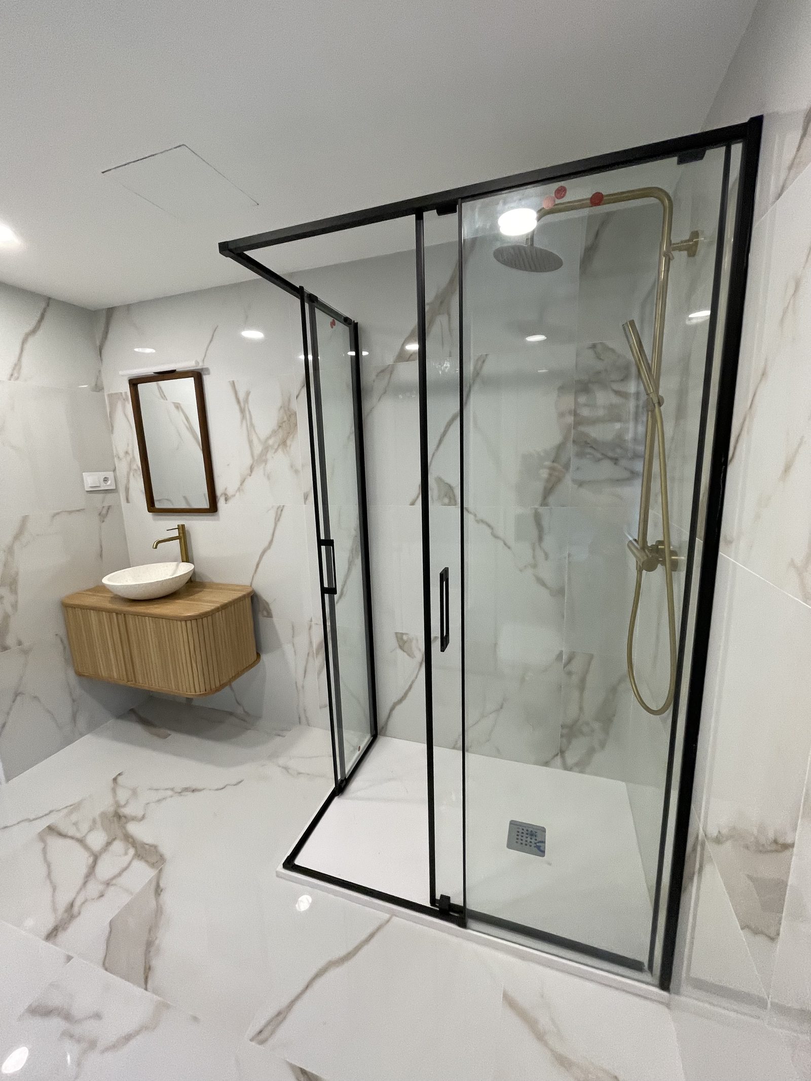 Baño reformado con mampara de vidrio, mármol y grifería de latón